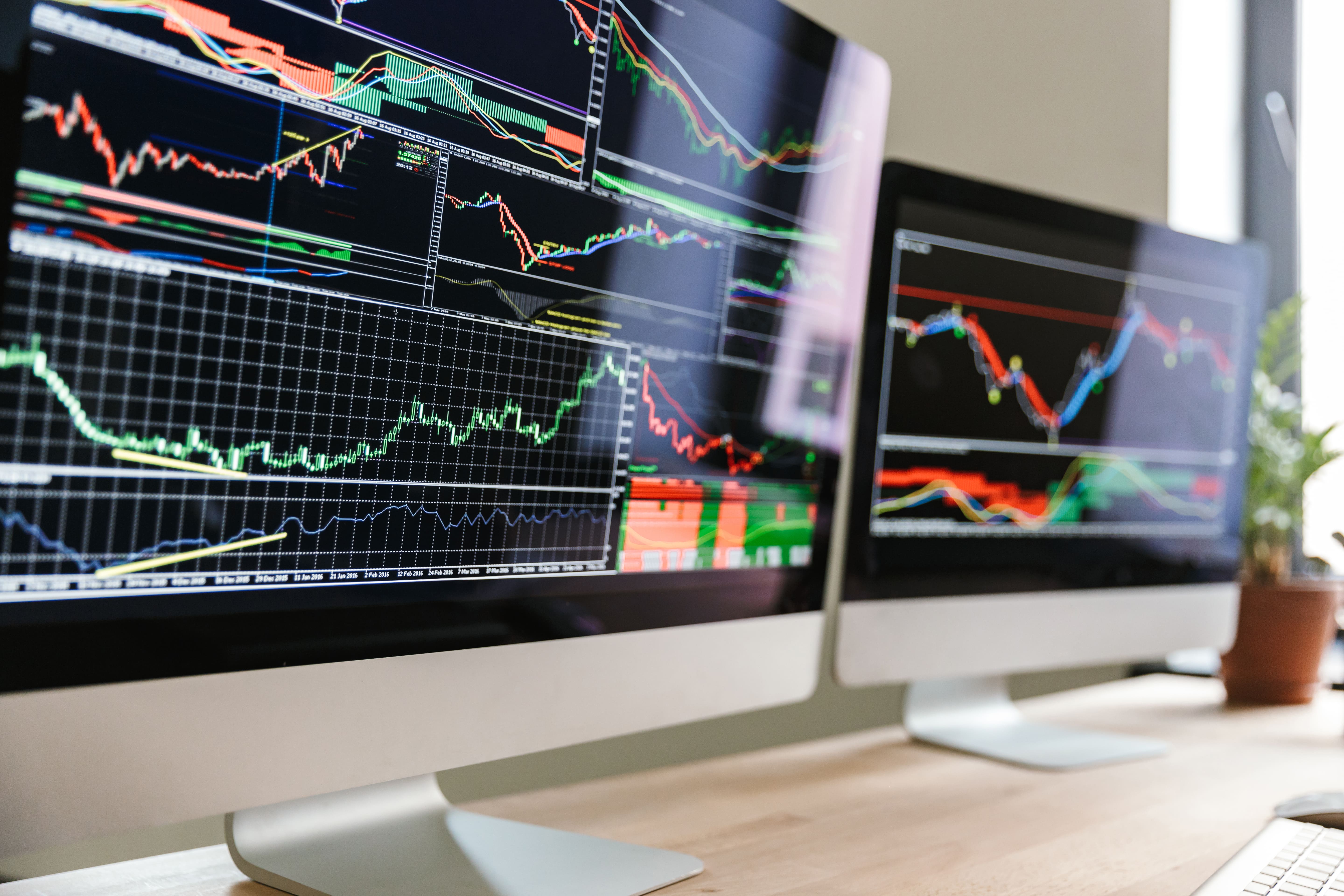 2 computer monitors showing financial market instruments graphs or candlesticks.