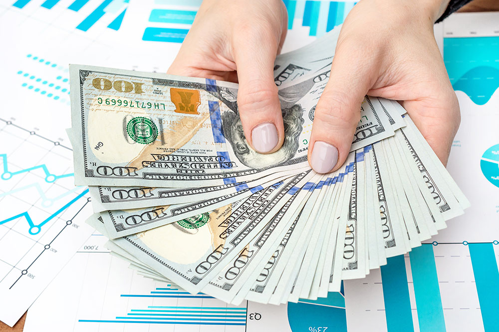 Forex trading image. A hand of a woman holding U.S. 100-dollar bills spreading them like a fan. Underneath are Forex financial graph papers.